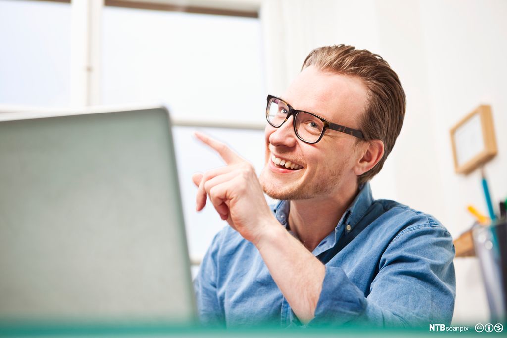 En glad ung mann sitter foran en datamaskin. Foto.