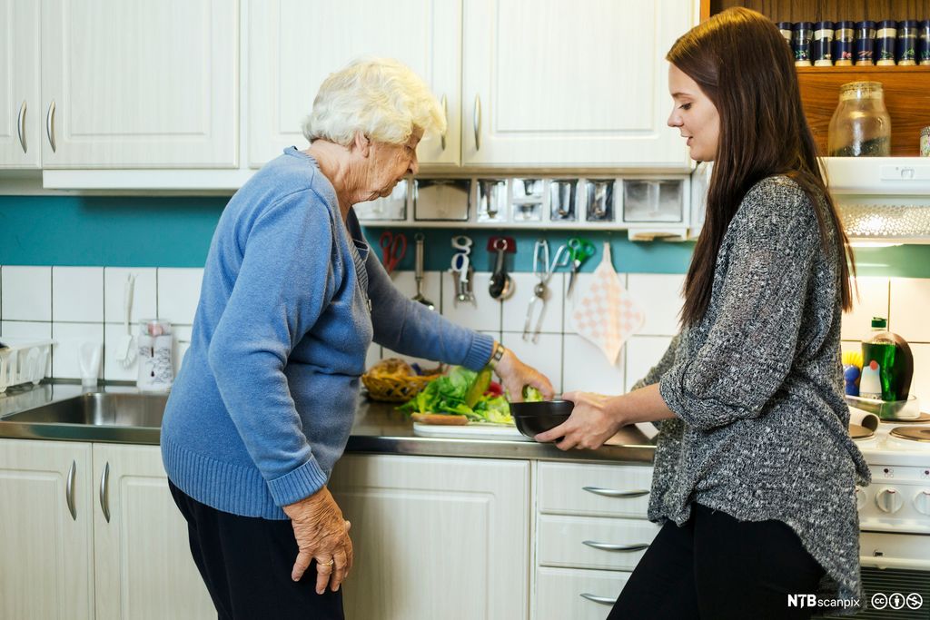 Eldre kvinne som får hjelp av en ung kvinne til å lage mat på kjøkkenet i et privat hjem. Foto