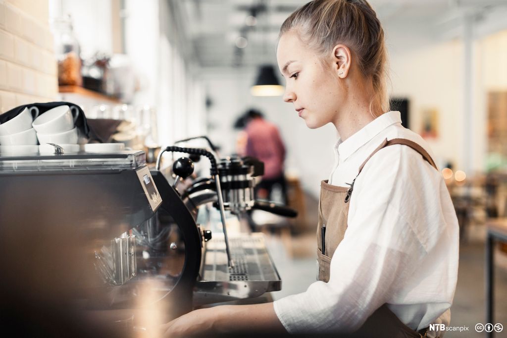 Ung person ved kaffemaskin. Foto.