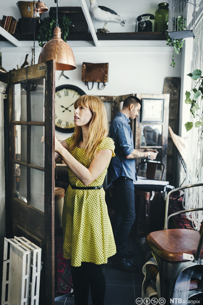 Mann og kvinne ser på retro-møbler i en interiørbutikk. De står med ryggen til hverandre og studere ulike varer. Foto.