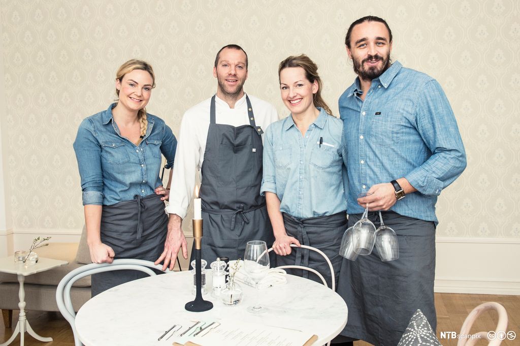 Fire ansatte i uformell uniform står ved bord i restaurant. Foto.