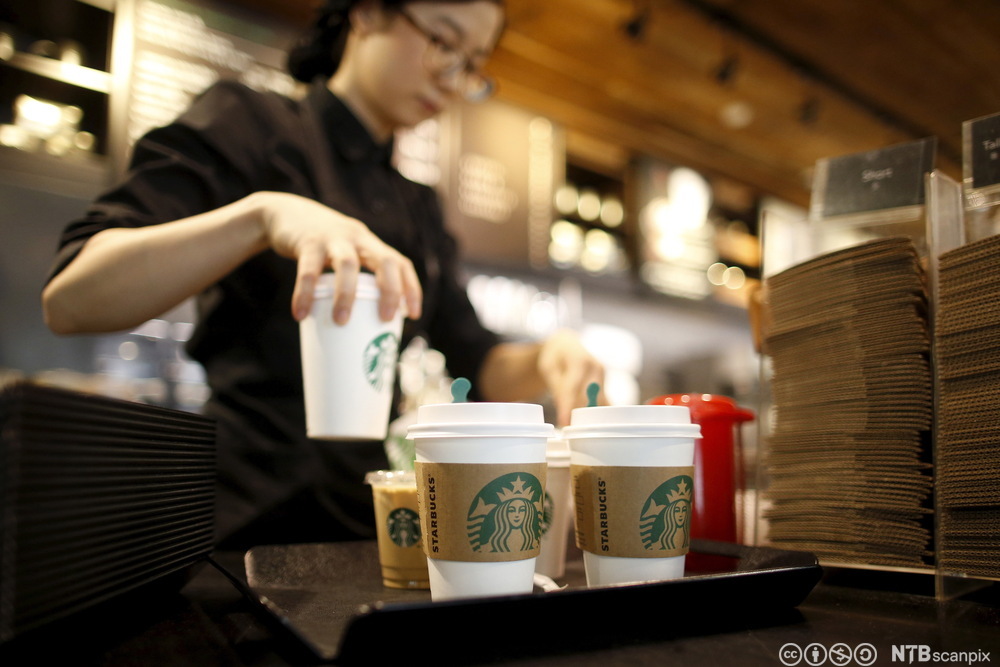 Person serverer kaffe i engangskopper. På koppene står det Starbucks. Foto. 