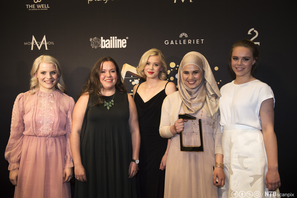 Foto av fem unge, kvinnelige skuespillere som smiler og holder statuetten de har vunnet under en prisutdeling.