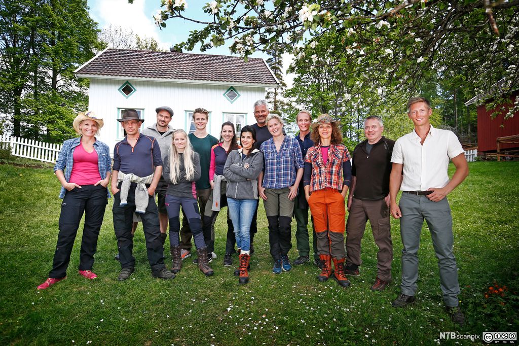 Ei gruppe kvinner og menn i fritidsklede framfor eit lite gardsbruk. Foto.