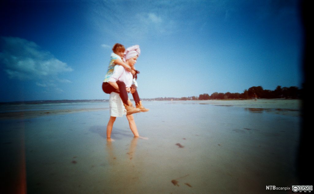 Ei jente bærer ei anna jente på stranda. Foto.