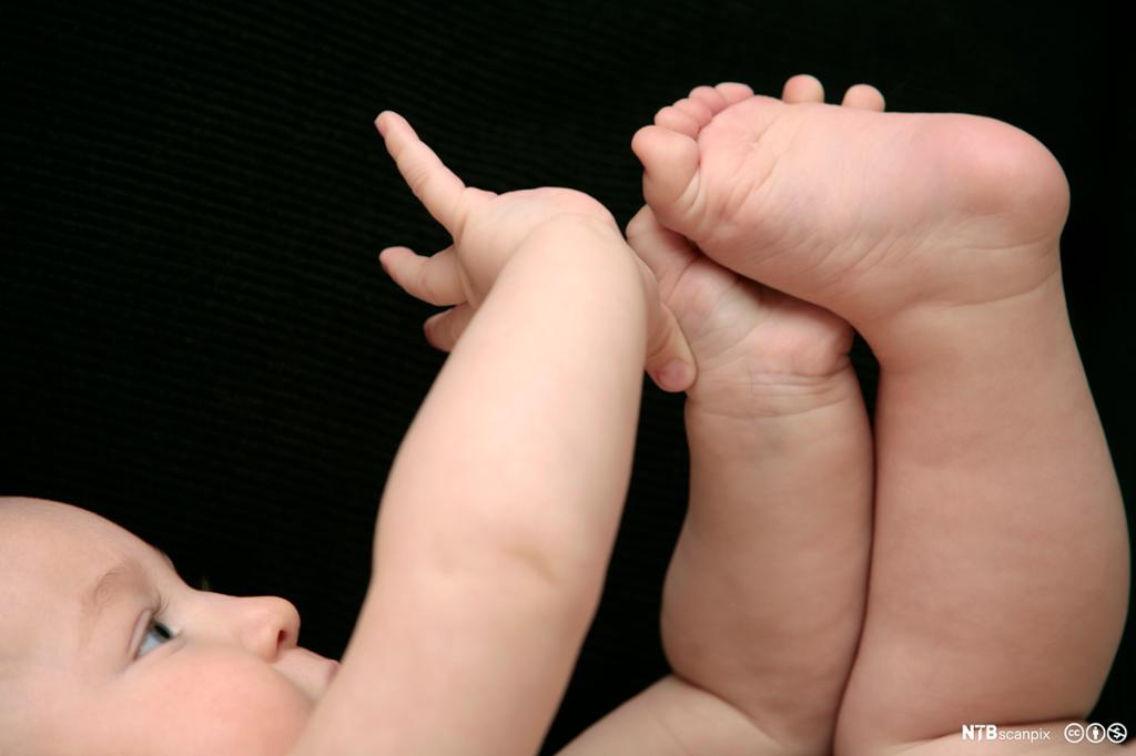 Naken baby som  leker med tærne sine. Foto.