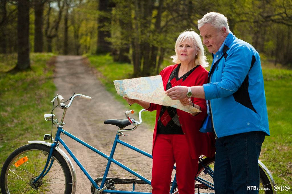 Eldre par med tandemsykkel studerer et kart. Foto.
