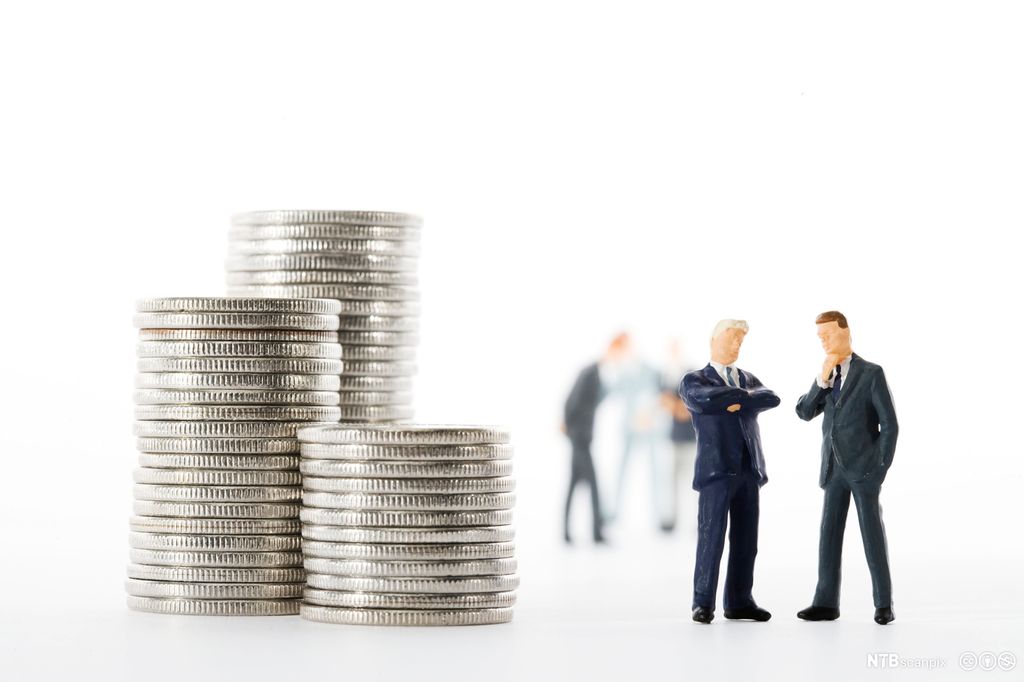 Tre myntstablar til venstre og to små figurar av menn i dress til høgre. Foto.