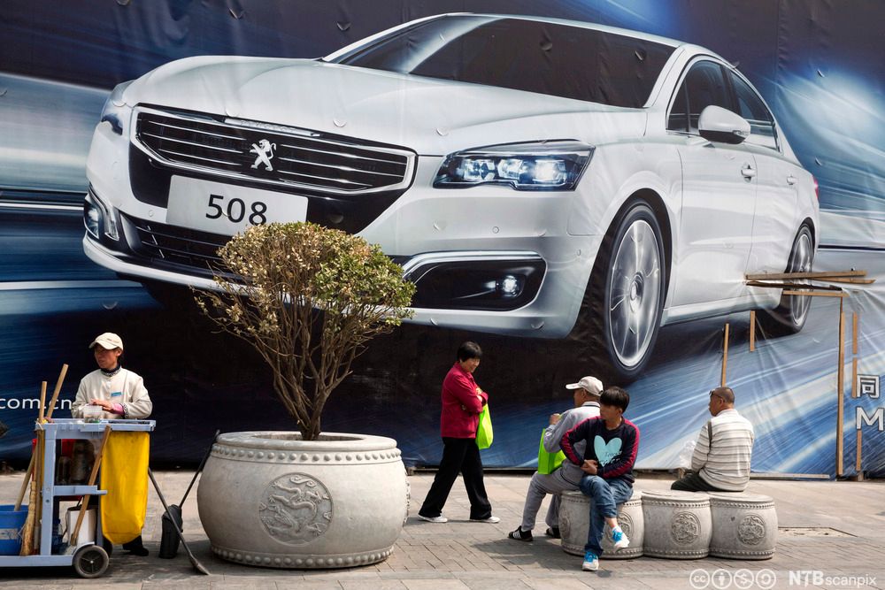 Mennesker passerer en reklamevegg for Peugeot på en åpen plass i Beijing. Foto.