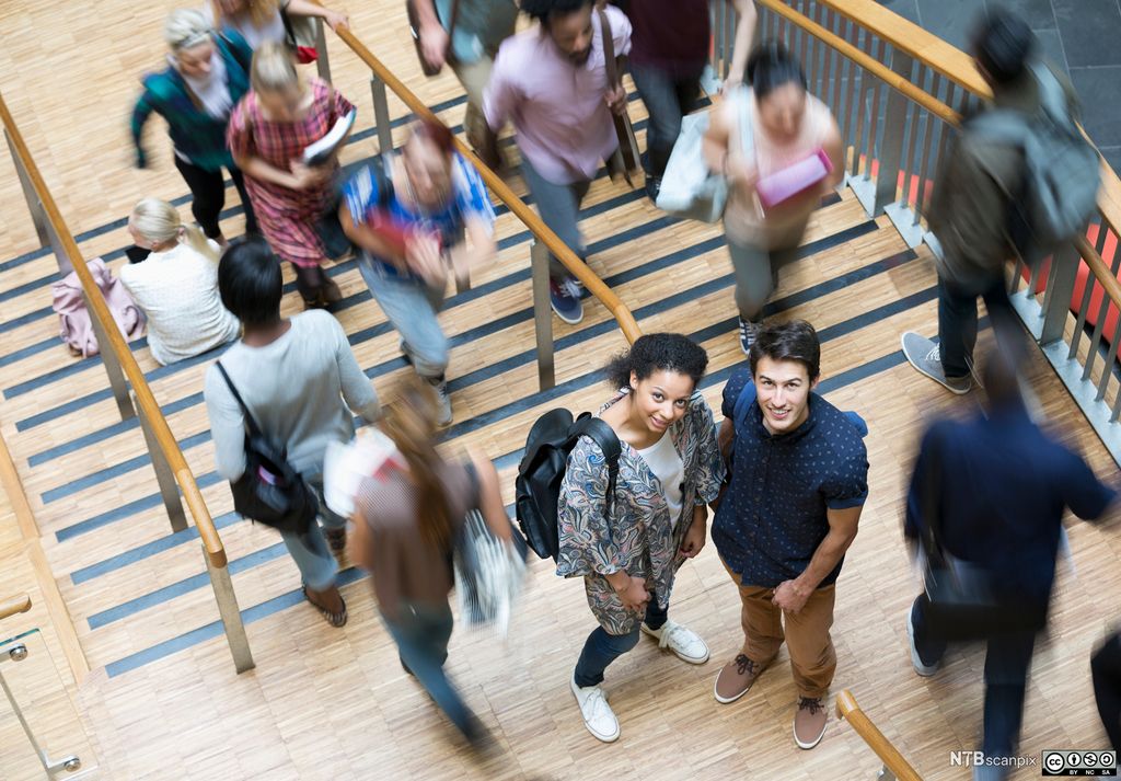 Studenter på vei opp eller ned ei brei trapp. To studenter står midt i trappa og ser opp mot kamera. Foto.