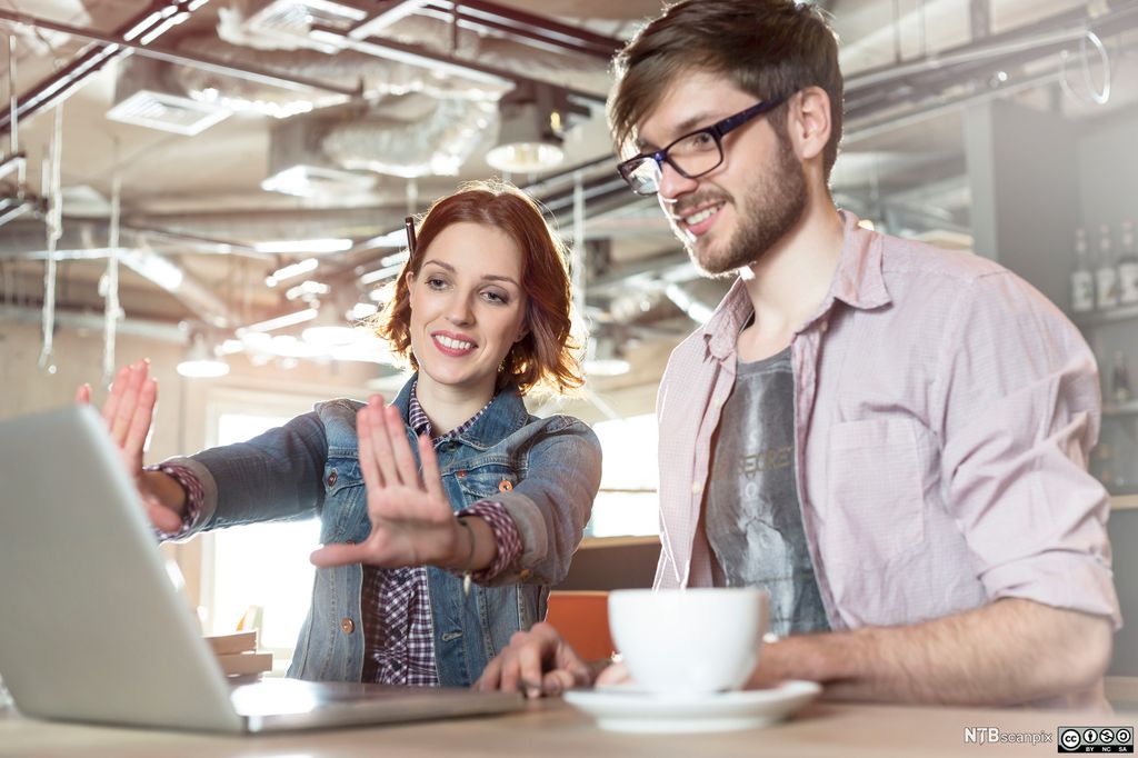 En mann og en kvinne ser på skjermen på en bærbar datamaskin. Kvinnen har en penn bak øret og holder håndflatane opp foran datamaskinskjermen. De smiler. Foto.