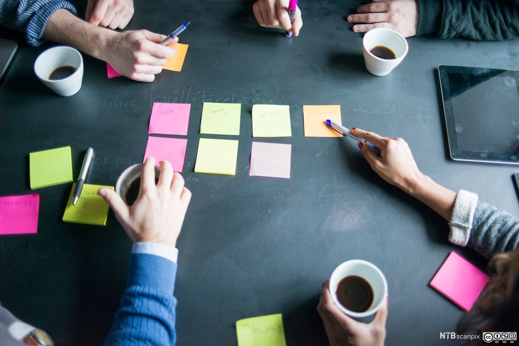 Armer som samarbeider over et bord med post-it-lapper. Foto.