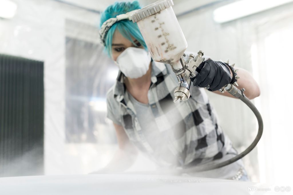 Kvinne med ansiktsmaske spraymaler en bil. Foto.