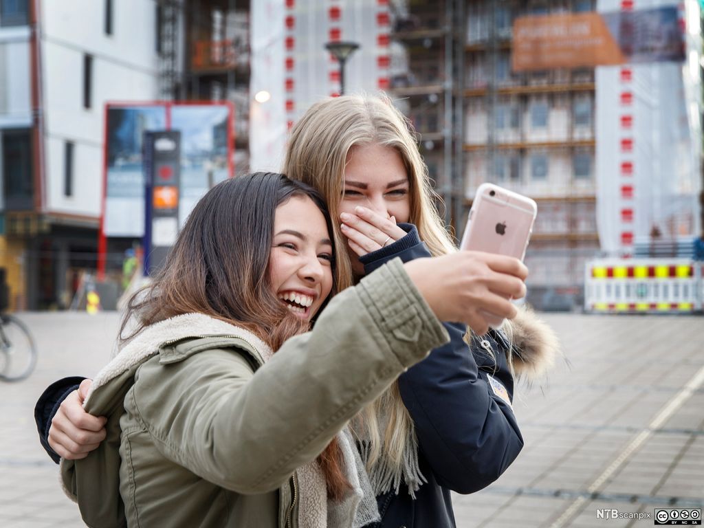  To jenter som tar en selfie. De to ler. Foto.