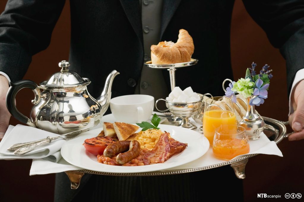 Butler serverer engelsk frokost på brett. Foto.