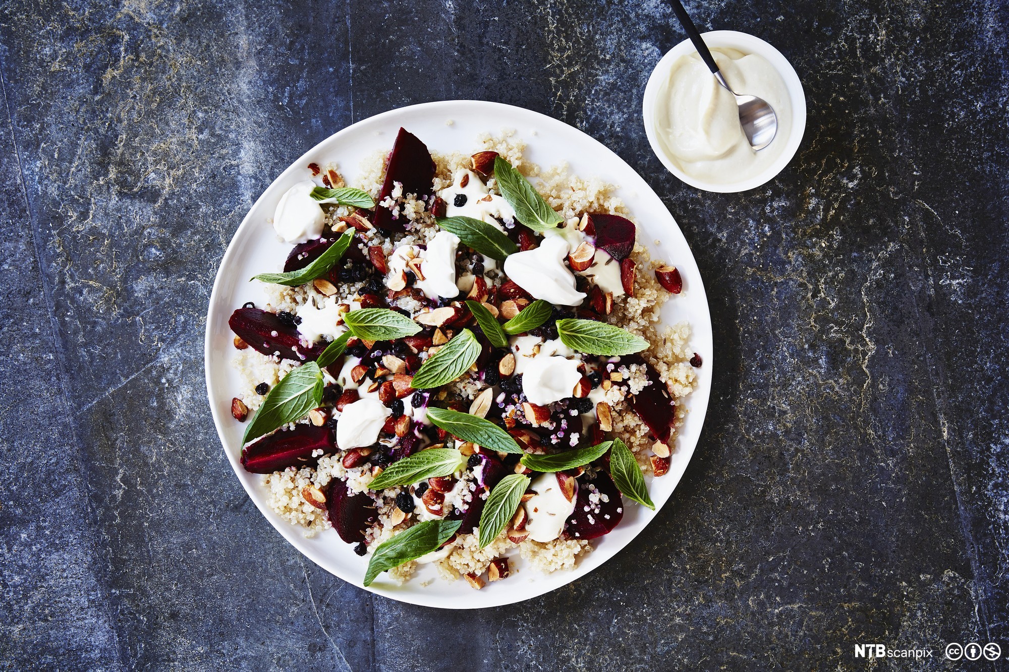 En salat av beter og quinoa på en tallerken. Ved siden av står ei skål med hvit dressing. Foto.