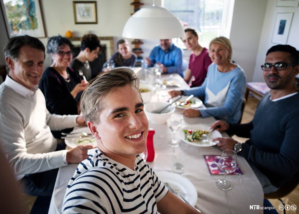 En tenåringsgutt sammen med familie og venner rundt et middagsbord. Foto.