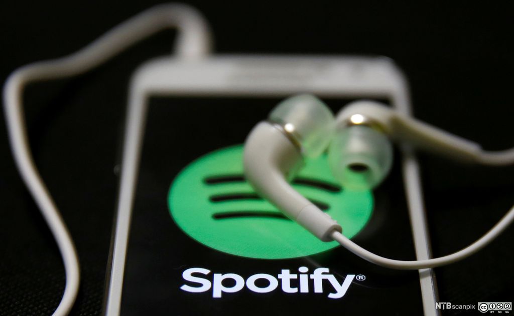 Spotify-logoen på en smarttelefon med høretelefoner liggende oppå. Foto.