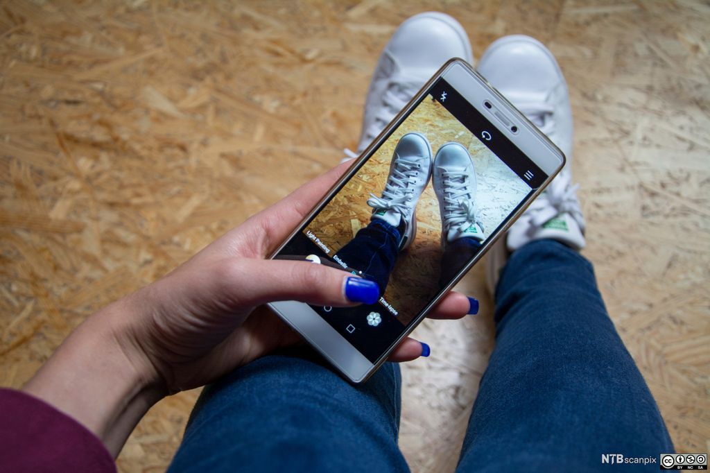 En ung jente tar bilde av joggeskoene sine med mobiltelefon. Foto.