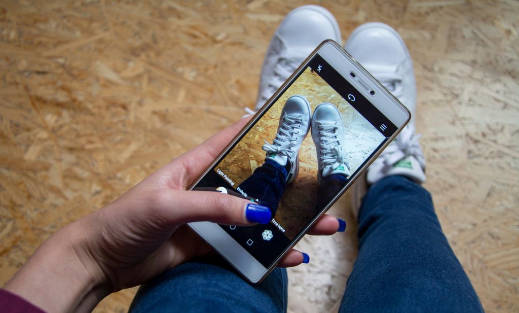 En ung jente tar bilde av joggeskoene sine med mobiltelefon. Foto.