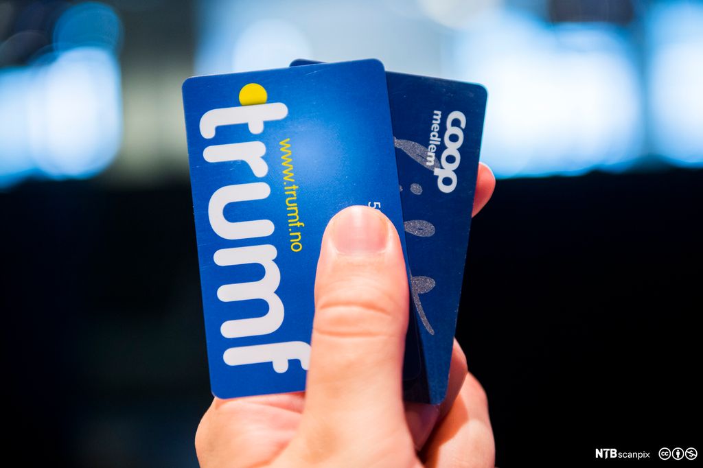 En hånd viser frem medlemskort fra Trumf og Coop. Foto.