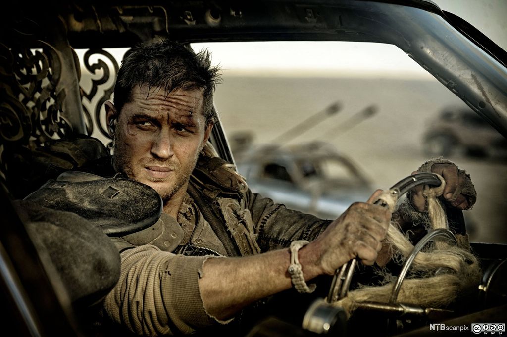 En skitten og såret mann i slitte klær sitter i en bil. Foto.