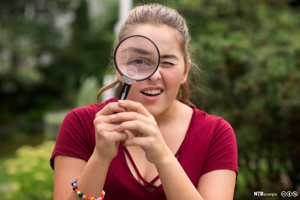 Ei jente holder et forstørrelsesglass foran det ene øyet. Foto.