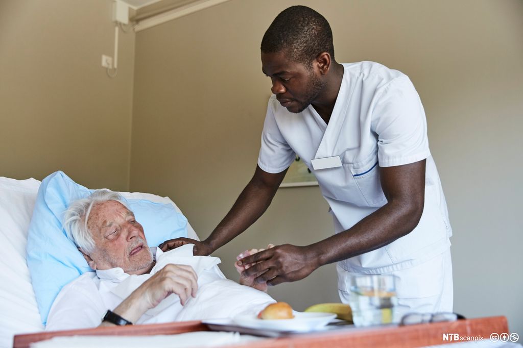 Mannlig sykepleier steller en gammel pasient. Foto.