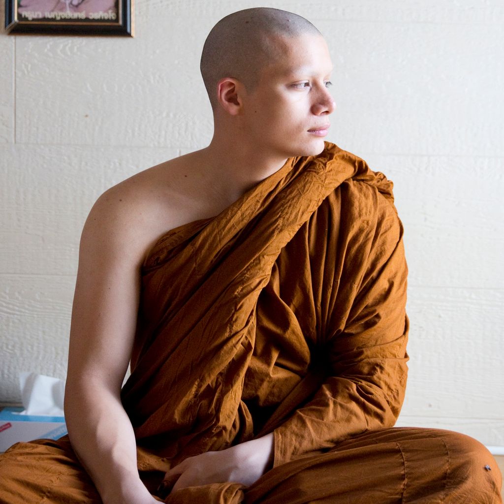 En ung buddhistmunk med gul kjortel stirrer ut av vinduet. Foto.