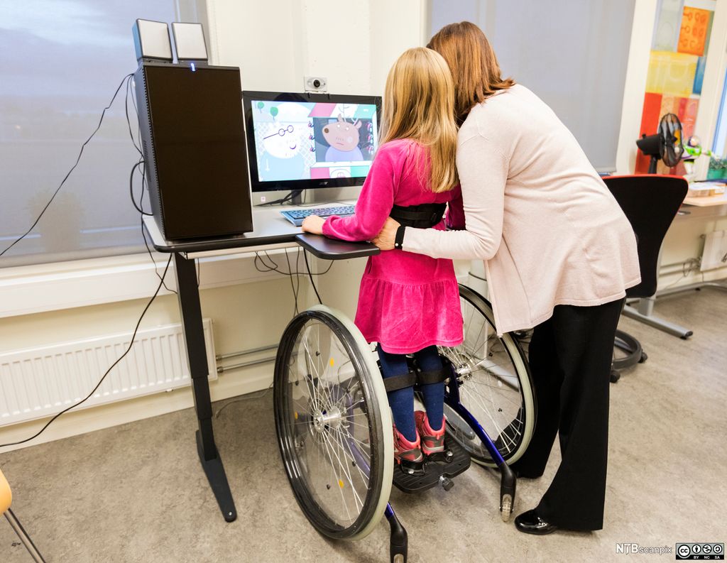 Voksen og barn står ved datamaskin. Foto. 