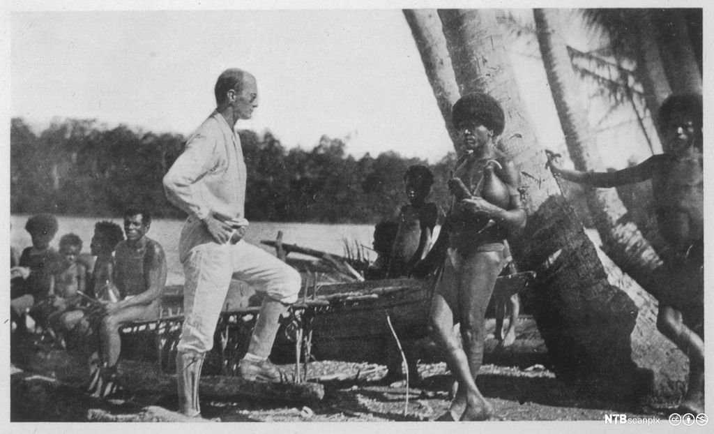 Antropologen Bronislaw Malinowski på Trobiandøyene. Han er en hvit mann kledd i lyse klær blant en mørkhudet folkegruppe. Foto. 