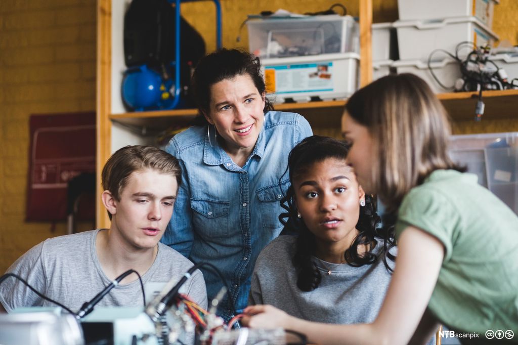 Multi-etnisk gruppe med elever diskuterer mens de gjør et eksperiment i klasserommet. Foto