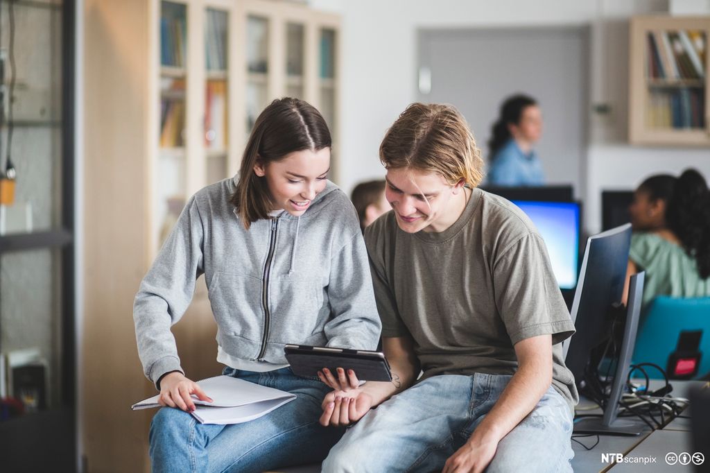 Хлопчик і дівчина сидять за столом і дивляться на планшет. Фото