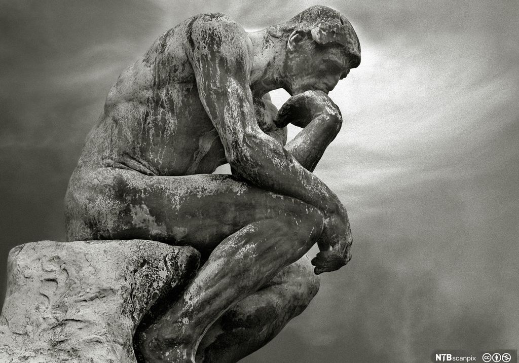 Statue av naken mann som sitter på en stein. Han støtter hodet med den ene hånden. Skulptur.