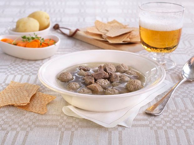 En tallerken trøndersodd og et glass øl servert med ulikt tilbehør ved siden av: poteter, flatbrød og gulrøtter. Foto.