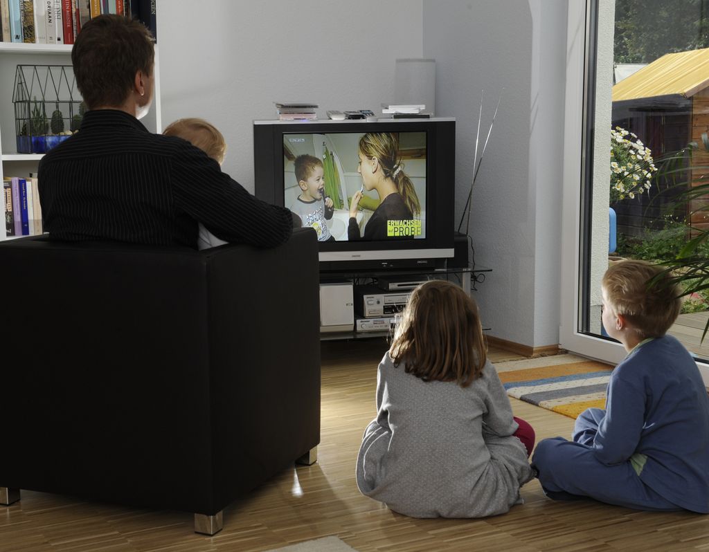 En forelder og tre barn sitter og ser på tv. Foto.