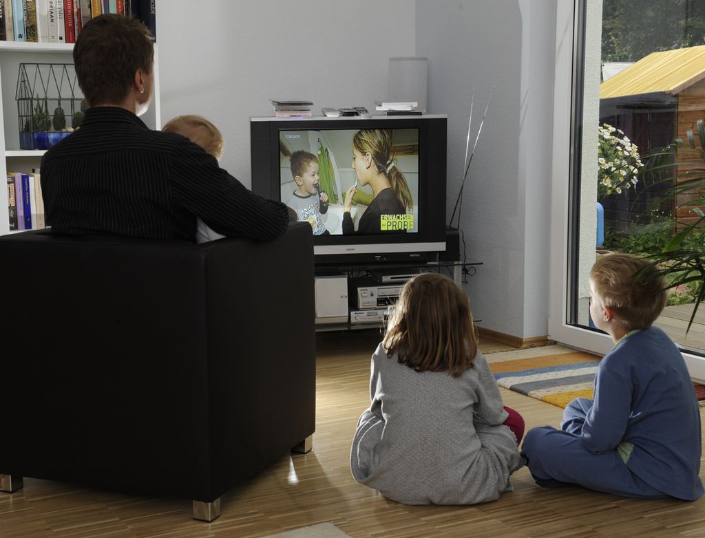 Ein forelder og tre barn sit og ser på tv. Foto.