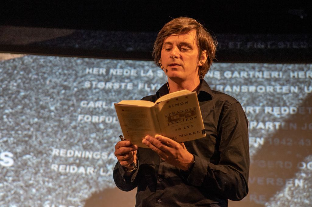 Mann med bøylemikrofon leser fra ei bok. Foto.
