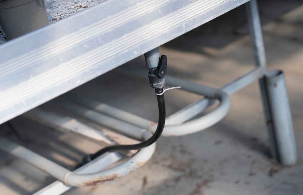 Slange med kran som er montert til et veksthusbord. Foto.