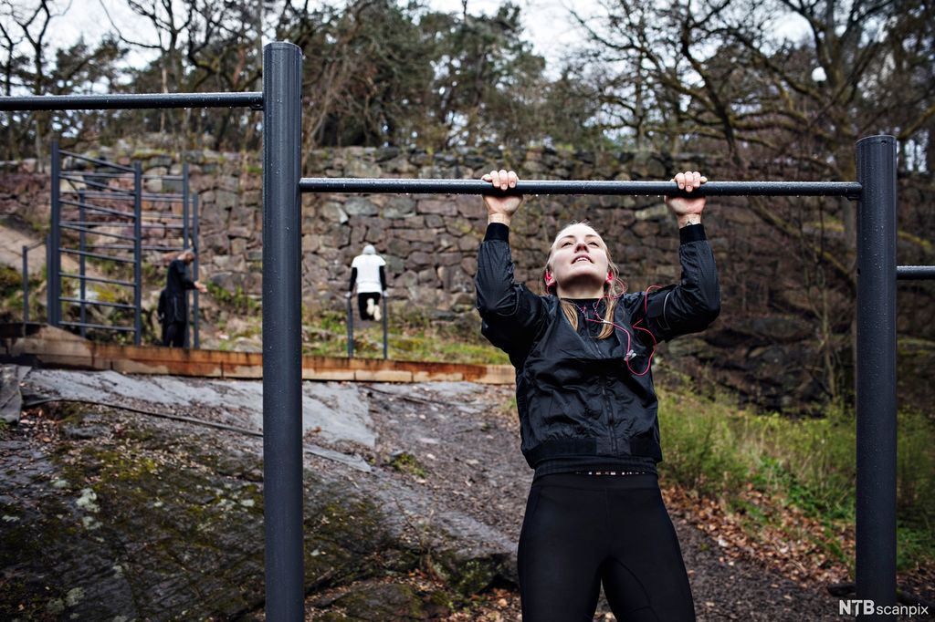 Ei jente henger i en vannrett stang i naturen. Foto.