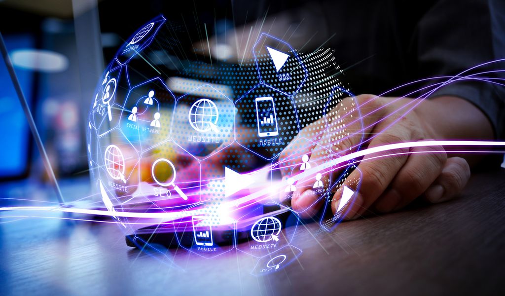 Bilde satt sammen av en hånd i bakgrunnen og en datategnet fotballaktig kule med ulike symboler for digital kommunikasjon på i forgrunnen. Illustrasjon.