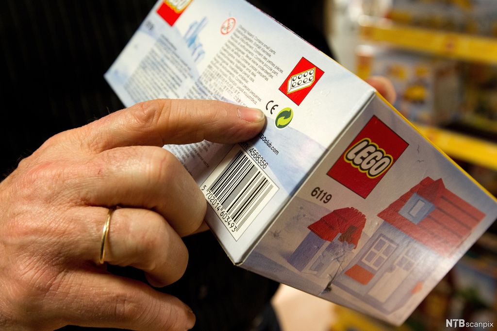 Finger peker på skrift på eske med LEGO. Foto.