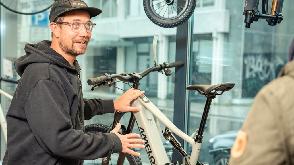 Sykkelselger står og demonstrerer og snakker med en kunde ved siden en utstilt elektrisk MTB-sykkel. Foto.