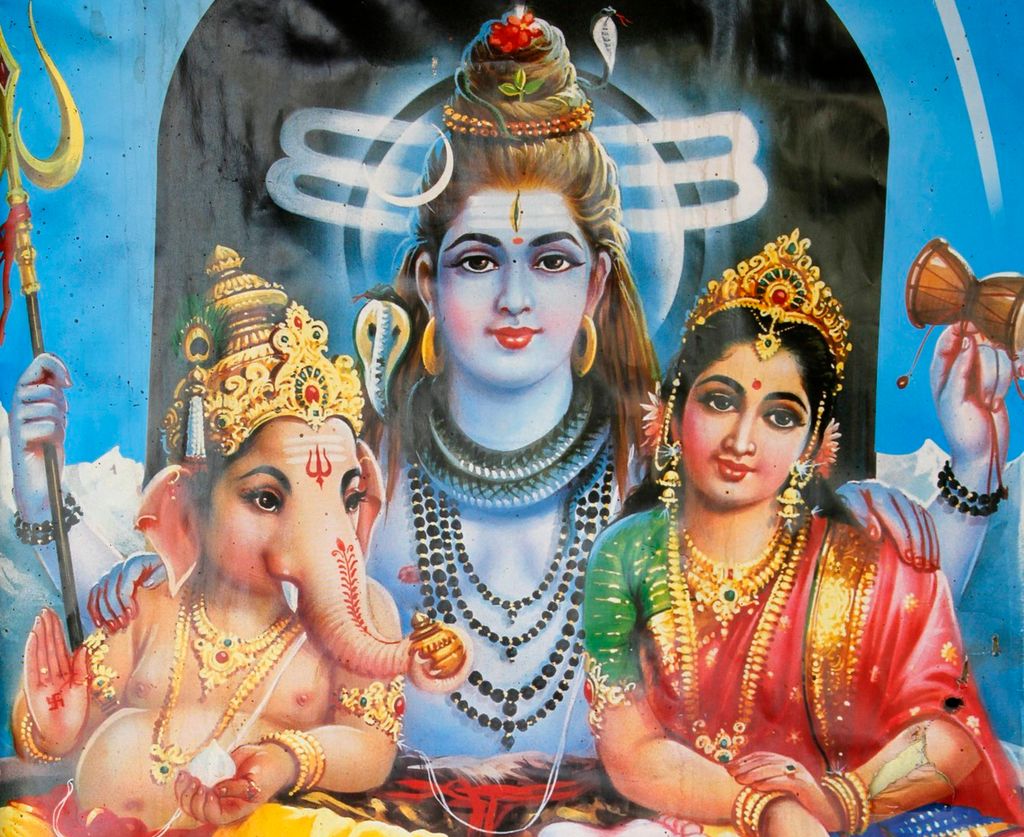 Tre sittande skikkelsar. Skikkelsen i midten er størst. Til venstre er ein skikkelse med elefanthovud og til høgre ein kvinneskikkelse. Begge lener seg mot den som sit i midten. Alle er rikt utsmykka og held ulike gjenstandar. Til dømes held skikkelsen i midten ein trefork og ei lita tromme. Illustrasjon.