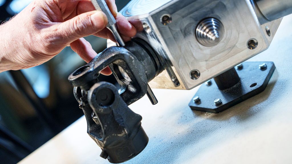 Hånd som holder et sølvfarga sylindrisk verktøy gjennom en ledda del. Foto.