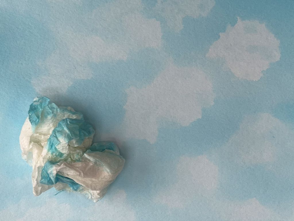 Detalj fra akvarell. Et sammenkrøllet tørkepapir med maling ligger oppå ei malt flate som gir inntrykk av skyer på en himmel. Foto.