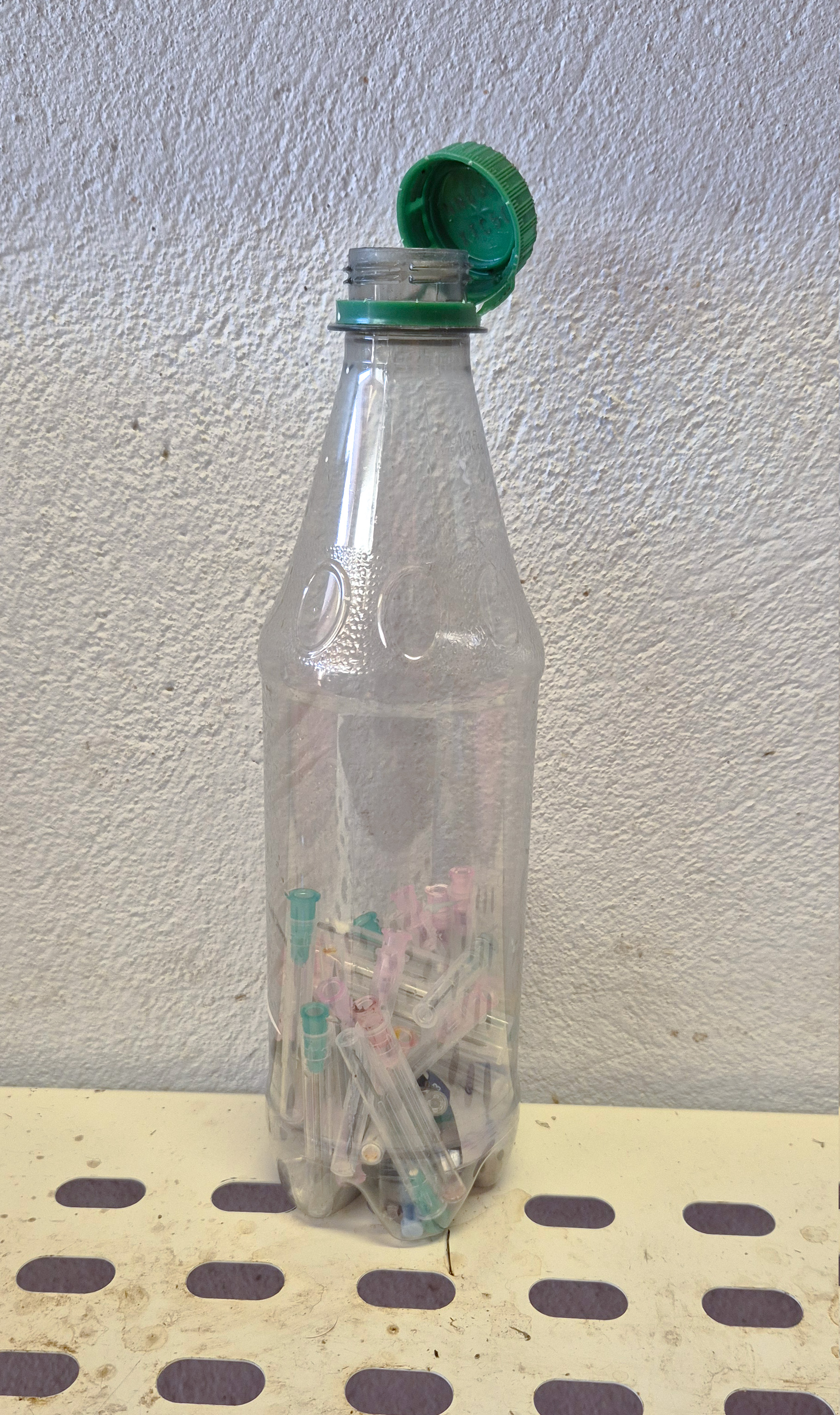 Ei brusflaske som er nesten halvfull av brukte sprøytespisser. Foto.