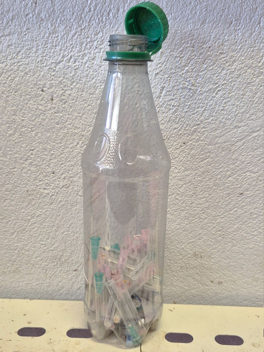 Ei brusflaske som er nesten halvfull av brukte sprøytespisser. Foto.