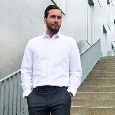 Pent kledd mann står i ei trapp og ser mot høyre. Foto.