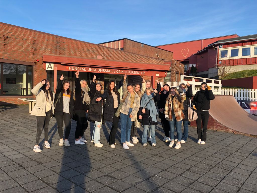 Videregående-elever står utenfor en ungdomsskole. Alle er jenter. De er blide og glade og viser tommel opp. Foto.